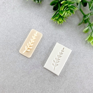 Peut inclure: Deux moules en silicone blanc pour l'artisanat, chacun présentant un motif en relief d'une seule brindille de feuilles.