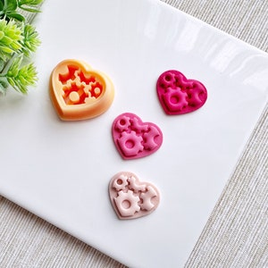 May include: Four heart-shaped silicone moulds with a gear design. The moulds are in shades of pink and orange.