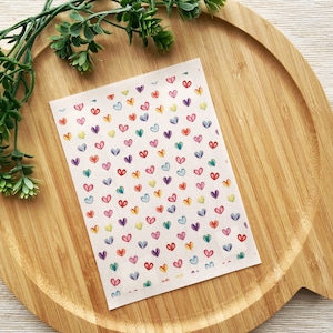 May include: A sheet of colorful heart stickers. The hearts are arranged in rows and are in various shades of pink, purple, blue, green, yellow, and orange.