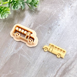 Op de afbeelding: Twee beige plastic koekjessnijders in de vorm van een schoolbus. Eén is de omtrek, de andere een gedetailleerde busvorm. Deze uitstekers zijn ontworpen voor bakken en knutselen.