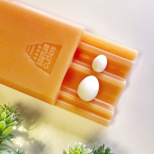 May include: Orange plastic mould with the text "BABYLON cutters" and two white round soap bars inside.