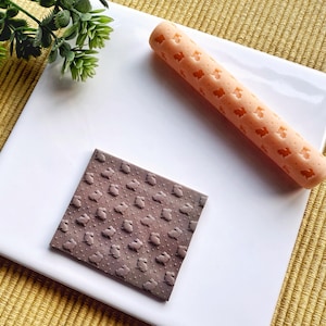 Può includere: Un mattarello in silicone rosa con un motivo a coniglietto ripetuto. È mostrato anche un pezzo quadrato di cioccolato con un motivo a coniglietto simile.