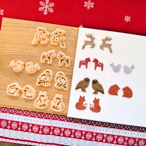 Könnte beinhalten: Eine Sammlung von weihnachtlichen Ausstechformen und dekorativen Formen. Die Ausstecher haben die Form von Rentieren, Pferden, Vögeln, Eulen, Füchsen und Igeln. Die Formen sind in Braun-, Rot- und Grautönen gehalten. Die Artikel befinden sich auf einem Holzbrett und einer weißen Oberfläche.