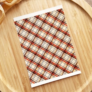 May include: A sheet of patterned paper with a plaid design in shades of red, brown, beige, and white.
