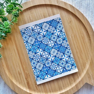 May include: A white card featuring a blue and white geometric pattern. The design is made up of squares and diamonds, reminiscent of traditional Portuguese tiles.
