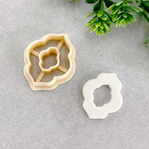 May include: Two plastic cookie cutters in the shape of a flower. The larger cutter is open and the smaller cutter is closed.