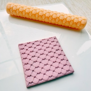 May include: A set of two pink silicone rolling pins with a scale pattern. The rolling pins are used for decorating cakes and pastries.