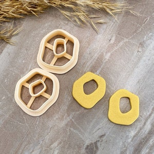 May include: Two cookie cutters in the shape of a rounded rectangle with a smaller rounded rectangle inside. Two yellow cookie dough shapes in the same shape as the cookie cutters.