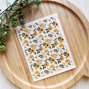 Peut inclure: Une feuille de papier blanc avec un motif répétitif de fleurs jaunes et vertes. Les fleurs sont stylisées et ressemblent à des tournesols.