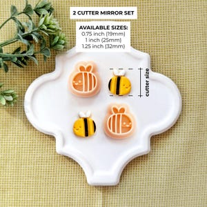 Pode incluir: Quatro cortadores de biscoitos em forma de abelha, dois de cada desenho, em um conjunto espelhado. Os cortadores s&atilde;o de cor p&ecirc;ssego claro, com abelhas listradas em amarelo e preto. Tamanhos dispon&iacute;veis: 19 mm, 25 mm e 32 mm. O texto diz: '2 CUTTER MIRROR SET'.