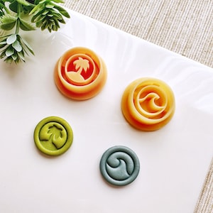 Könnte beinhalten: Vier Wachssiegel mit verschiedenen Designs. Ein Siegel ist grün mit einer Palme, eines ist orange mit einer Welle, eines ist orange mit einer Palme und eines ist blau mit einer Welle.