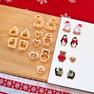 Könnte beinhalten: Eine Sammlung von weihnachtlichen Ausstechformen und dekorativen Magneten. Die Ausstechformen haben die Form eines Weihnachtsmanns, Weihnachtsbaums, Pullovers, Bären und Pinguins. Die Magnete zeigen Pinguine, einen Bären, ein Rentier und Katzen mit Weihnachtsbäumen.