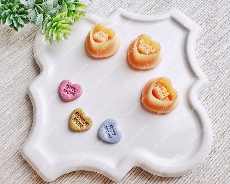 May include: Five heart-shaped candy molds with different messages: "Girl Mom", "Bonus Mom", "Boy Mom", "You Mom", and "Super Mom". The molds are made of a clear, flexible plastic and are perfect for making homemade candy.