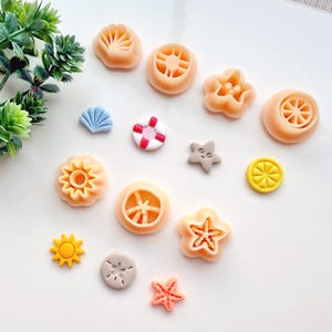 May include: A collection of 13 small, colorful, and detailed polymer clay charms with summer and beach themes. The charms include a seashell, a starfish, a life preserver, a sun, a lemon, an orange, and a flower.