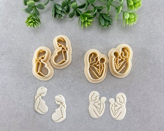 Puede incluir: Conjunto de seis cortadores de galletas con forma de mujeres embarazadas y madres que sostienen bebés. Los cortadores están hechos de un material plástico beige.