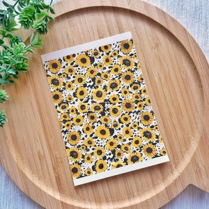 May include: A white card with a pattern of yellow sunflowers on a black and white background. The card is on a wooden surface.