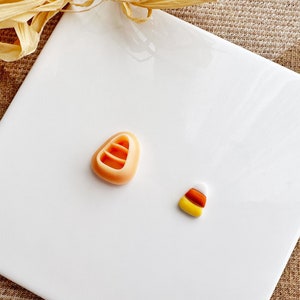 Könnte beinhalten: Zwei Halloween-förmige Süßigkeitenformen auf einer weißen Oberfläche. Eine Form ist wie ein Maisbonbon geformt und die andere wie ein traditionelles Maisbonbon.