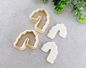 Op de afbeelding: Een bovenaanzicht van twee beige plastic koekjessnijders in de vorm van een zuurstok en twee witte zuurstokvormige koekjes. De koekjessnijders hebben een golvende rand. De koekjes zijn glad en wit. De achtergrond is een lichtgrijze ondergrond.