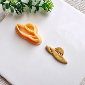 May include: Two cookie cutters in the shape of a sun hat. The larger cutter is a light orange colour and the smaller cutter is a light brown colour.