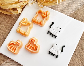 Puede incluir: Un juego de cortadores de galletas con temática de Halloween. Los cortadores están hechos de plástico naranja y presentan un fantasma, un gato y un vestido.