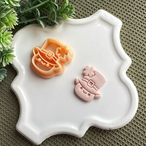 Może przedstawiać: Dwie różowe i pomarańczowe dekoracje z lukru w kształcie krasnoludków w kapeluszach. Dekoracje znajdują się na białym ceramicznym talerzu z falistym brzegiem.