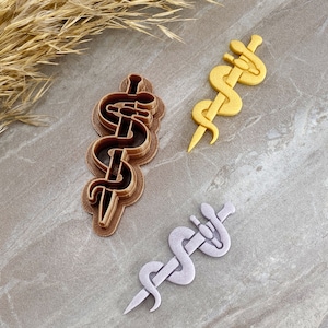 May include: Three 3D printed medical caduceus symbols. One is brown, one is yellow, and one is light purple.