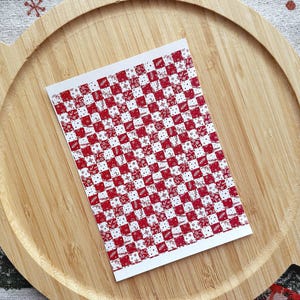 Op de afbeelding: Een vel met rode en witte geruite stickers met een wit sneeuwvlokkenpatroon.