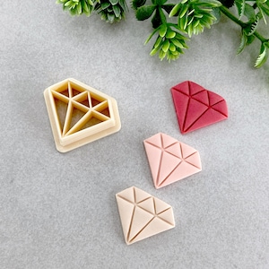 May include: Three diamond-shaped cookie cutters, one beige, one pink and one red. The cutters are on a grey surface.