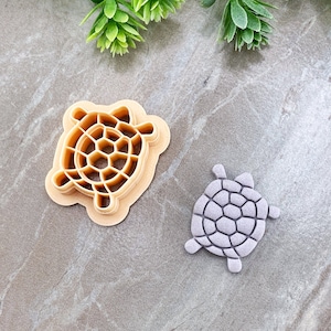 Peut inclure: Deux emportes-pièces en forme de tortue en plastique. L'un est beige et l'autre est violet clair.