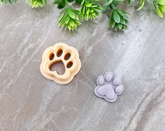 May include: Two plastic paw print cookie cutters. One is beige and the other is purple.