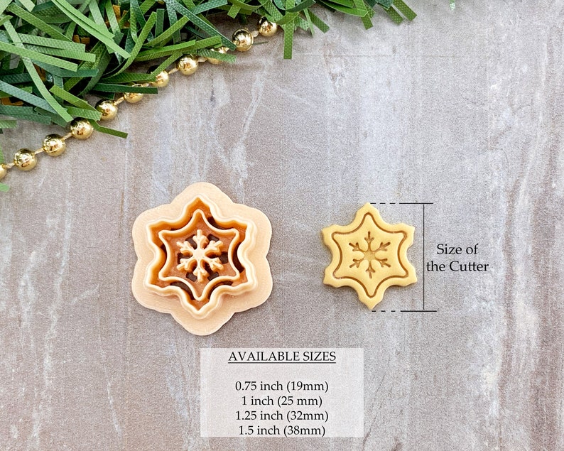 May include: Two snowflake cookie cutters, one larger and one smaller, on a light brown surface. The larger cutter is 1.5 inches (38 mm) in diameter and the smaller cutter is 0.75 inches (19 mm) in diameter.  AVAILABLE SIZES: 0.75 inch (19mm), 1 inch (25 mm), 1.25 inch (32mm), 1.5 inch (38mm).