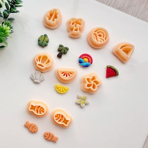 以下が含まれることがあります： 貝殻、花、魚、スイカの切り身、レモンの切り身、ヤシの木、パイナップル、夕焼け、虹、葉など、15種類のカラフルなポリマークレイの形状のセットです。 形状はすべてオレンジ、イエロー、グリーン、ブルー、レッド、ホワイトの色合いです。