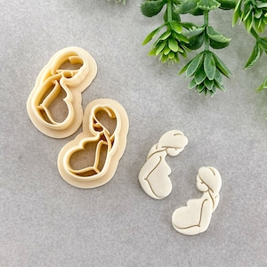 May include: Two cookie cutters, one shaped like a pregnant woman and the other shaped like a pair of flip flops.