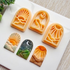 Op de afbeelding: Vijf siliconen mallen voor bakken of knutselen. De mallen zijn gevormd als gewelfde ramen met verschillende scènes erin. De scènes omvatten een opkomende zon boven wolken, een wassende maan en sterren, en een ondergaande zon boven bergen.