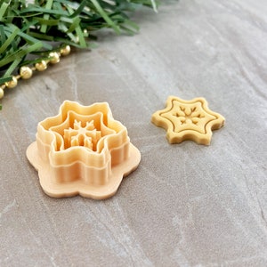 May include: Two plastic cookie cutters in the shape of a snowflake. The larger cutter has three layers, while the smaller cutter is a single layer.