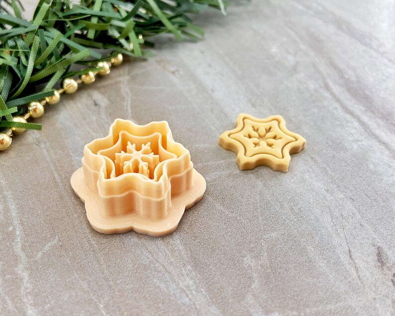 May include: Two plastic cookie cutters in the shape of a snowflake. The larger cutter has three layers, while the smaller cutter is a single layer.