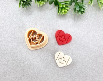 Può includere: Tre tagliabiscotti a forma di cuore, uno rosso, uno beige e uno bianco, ognuno con un design a foglia d'acero. I tagliabiscotti sono su una superficie grigio chiaro.