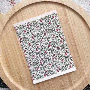 May include: A white card with a repeating pattern of green leaves and red berries. The pattern is reminiscent of a traditional Christmas design.