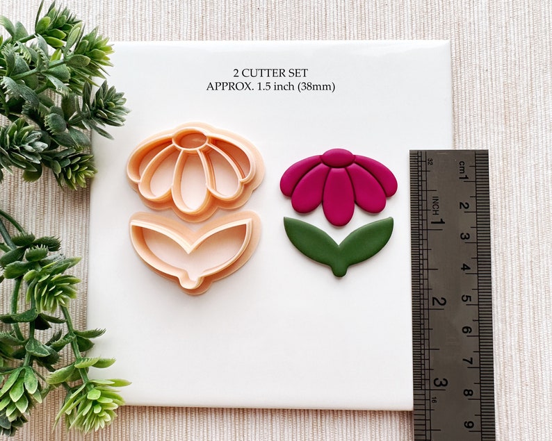 May include: A set of two cookie cutters, one for a flower with a single leaf and one for a flower with two leaves. The cutters are 1.5 inches in diameter. The flower cutter is beige and the leaf cutter is green.