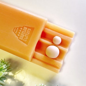 Peut inclure: Gros plan sur un ensemble de deux emporte-pièces en plastique orange dans un étui. L'étui est étiqueté "Babylon Cutters".