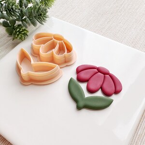 May include: A set of three cookie cutters in the shape of a flower, butterfly, and leaf. The flower cutter is pink, the butterfly cutter is orange, and the leaf cutter is green.