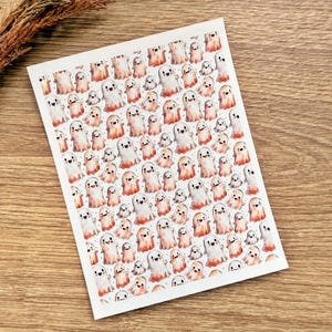 Op de afbeelding: Vel stickers met een herhalend patroon van lachende cartoongeesten. De geesten zijn wit met oranje accenten en kleine zwarte ogen. De stickers staan op een witte achtergrond.