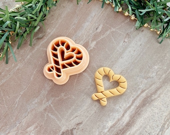May include: Two heart-shaped cookie cutters, one in a light brown color and the other in a darker brown color. Both cutters feature a candy cane design.