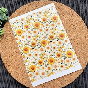 Può includere: Un foglio di carta bianca con un motivo ripetitivo di girasoli gialli e margherite bianche. Lo sfondo è bianco.