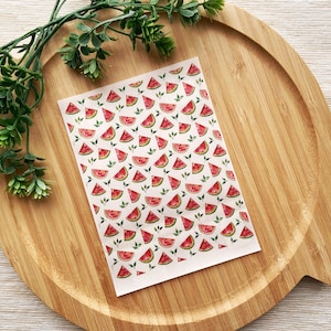 May include: A sheet of white paper with a repeating pattern of red watermelon slices and green leaves. The paper is on a wooden surface.