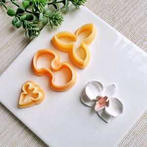 May include: A set of four cookie cutters in the shape of flowers. The cutters are made of a light orange plastic and are arranged on a white surface.