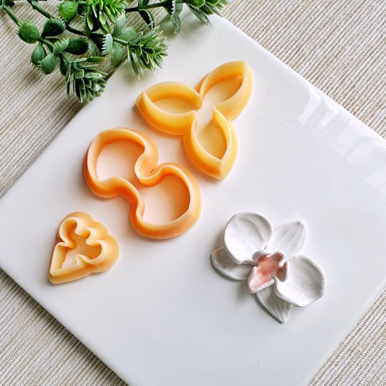May include: A set of four cookie cutters in the shape of flowers. The cutters are made of a light orange plastic and are arranged on a white surface.