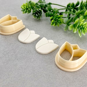 May include: Four plastic cookie cutters in the shape of a tulip. The cutters are in various sizes and are made of a cream-coloured plastic.