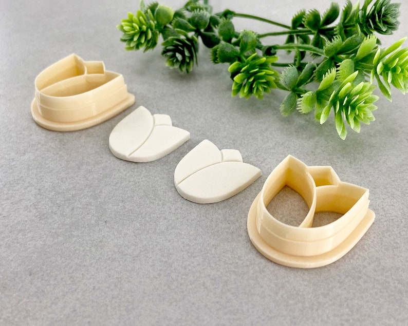 May include: Four plastic cookie cutters in the shape of a tulip. The cutters are in various sizes and are made of a cream-coloured plastic.