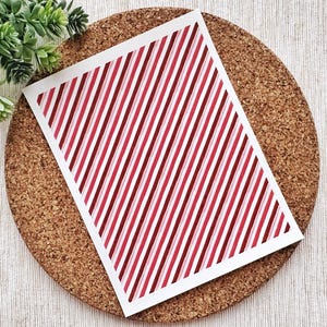 Könnte beinhalten: Ein weißes Blatt Papier mit einem diagonalen rot-weißen Streifenmuster. Das Papier liegt auf einer Korkoberfläche.